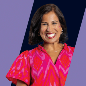 A smiling woman with dark hair, wearing a bright pink patterned dress, stands against a background split into dark blue and light purple diagonal sections.
